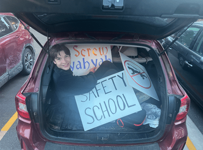 Carleton student in the trunk of a car with signs for a football game